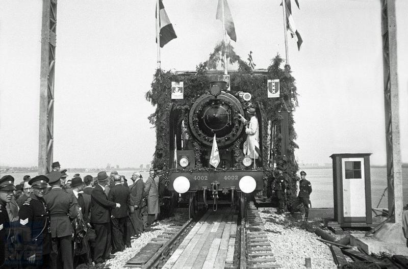 Groot feest: de Moerdijkbrug is hersteld! Op deze foto gaat een directietrein als eerste het Hollands Diep over en bereikt over enkele minuten Noord-Brabant. De trein wordt getrokken door stoomlocomotief 4002. Dit is een machine uit de serie 4001-4015 die na de oorlog uit Zweden het NS-locomotievenpark kwam versterken. Ze zijn gebouwd door Nohab in Trollhättan; bij de NS zijn het de enige 2C-locs met drie cilinders. (foto J.J.Overwater; 24-8-1946)