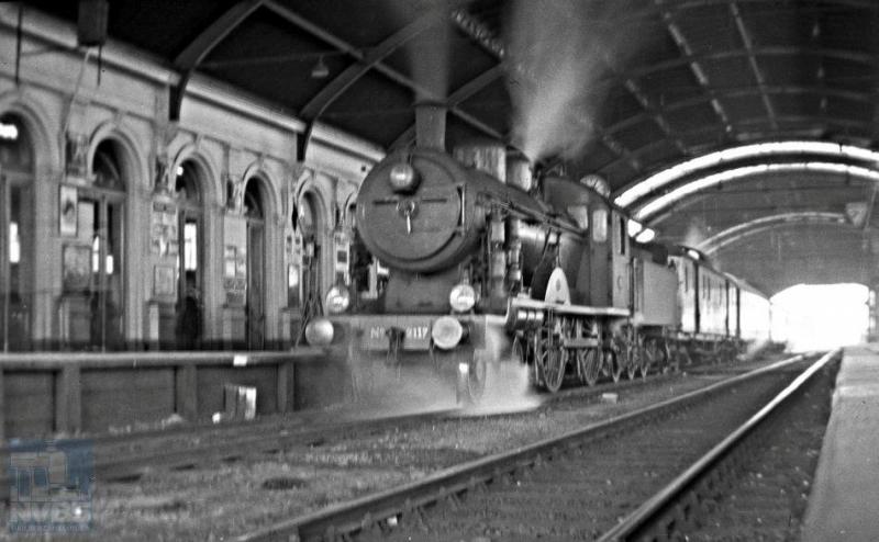 Een dag later fotografeerde Hesselink ongeveer op dezelfde plek een andere trein, nu duidelijk eentje in het personenverkeer. Een van de fraaiste locomotieven van de NS staat er voor: de 2B 2117 uit de serie 2101-2135. Bij de HSM hadden deze locs de nummers 501-535. De door Schwartzkopff in Berlijn vanaf 1914 gebouwde machines waren het antwoord van de HSM op de zware locs -de latere serie NS 3700- die de SS in dienst hadden gesteld. Ir. W.Hupkes heeft, met het Pruisische type S6 als voorbeeld, deze sneltreinlocomotief ontworpen met de maximaal toegestane asbelasting van 17 ton/as en met drijfwielen van 210 cm in doorsnee. Zijn alle passagiers al in- of uitgestapt? Geen mens te zien! 24 februari 1935 (NVBS-fotonummer 170.218).
