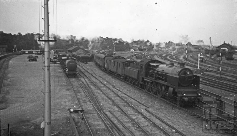 Aan de oostkant van het emplacement zien wij loc 3913 met internationale trein 111 vertrekken uit Amersfoort richting Duitsland. Het aantal personenrijtuigen was in die tijd, 6 augustus 1935, beduidend lager dan wat we nu in het internationale treinverkeer gewend zijn. Helemaal rechts op de foto kunt u het locomotievendepot nog zien.