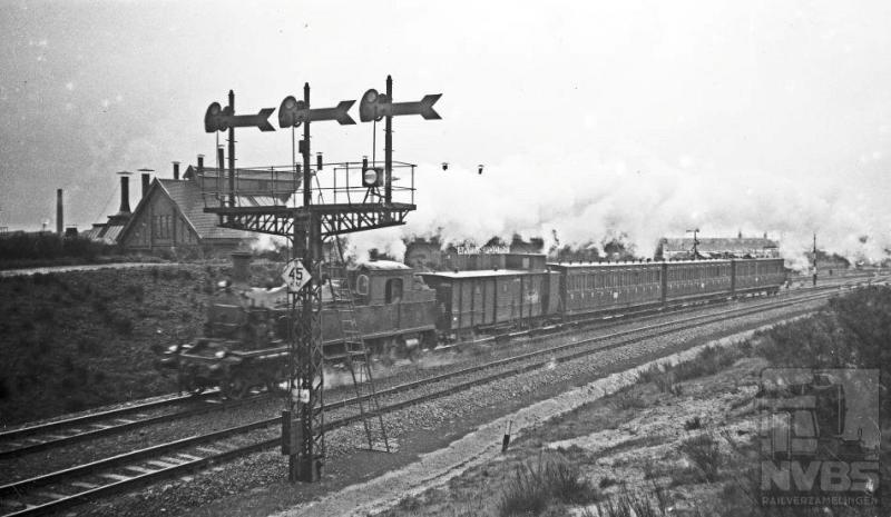 Aan de ene kant een drievoudig vertakkingsein, het inrijsein voor Amersfoort met bordje voor de toegestane snelheid en aan de andere kant een uit Amersfoort vertrokken reizigerstrein. De foto is niet helemaal scherp zodat het locnummer niet is te onderscheiden; het is er in ieder geval een uit de serie NS 5806-5812. Deze tenderlocs, gebouwd door Werkspoor, kwamen in 1915 in dienst bij de HSM. 3 mei 1936.