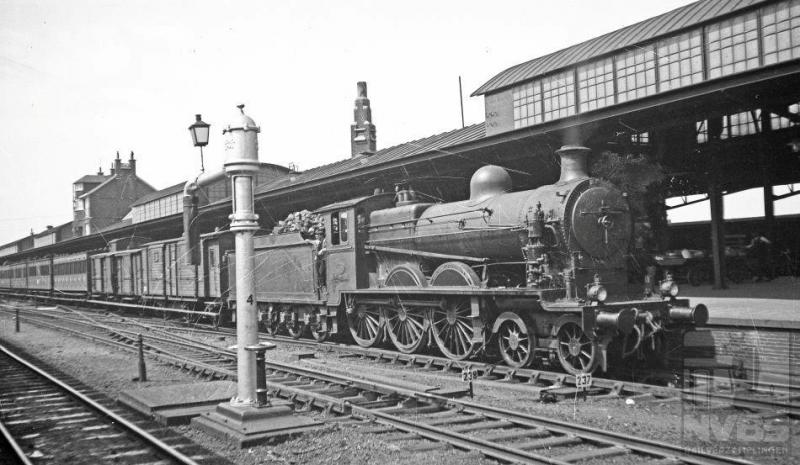 Op deze foto staat locomotief NS 3505 met een reizigerstrein langs het perron. Aan de andere kant zien we nog net een rijtuig van een internationale of sneltrein. De waterkolom op de voorgrond mag er ook zijn, met dat grappige lantaarntje bovenop. Deze 2C-locomotief, afkomstig van een kleine serie van acht stuks, kwam in 1908 in dienst bij de Noord-Brabantsch-Duitsche Spoorwegmaatschappij (NBDS), de kleinste die Nederland heeft gekend. Op ons grondgebied reden deze locs van Boxtel via Veghel en kruispunt Beugen naar de grens met Duitsland, waar het verder ging naar Gogh en Berlijn. Maar dan met een Duitse loc ervoor natuurlijk. Het is 12 augustus 1935.