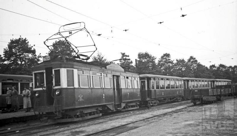 Een lange tram van een motorwagen (77) met drie aanhangwagens van de Nederlandsche Buurtspoorweg Maatschappij (NBM) is aangekomen op het tramstation van Amersfoort vanwaar het NS-station in een paar minuten is te bereiken. Bewoners van de streek tussen Zeist en Amersfoort konden sinds de elektrificatie van deze lijn in 1924 veel sneller het station bereiken. De 77 is van een serie van veertien door Werkspoor speciaal voor deze smalspoorlijn gebouwde vierassige motorwagens. Het rijtuig heeft zijn laatste jaren nog dienst gedaan bij de GETA. De NBM bestreek een groot gebied tussen Utrecht en Arnhem. Plaatsen als Zeist, Doorn, Amersfoort en Rhenen werden bediend.Foto: H.G. Hesselink (170.736A)