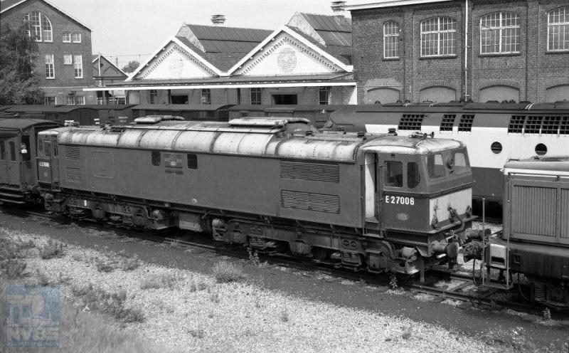In 1970 kocht NS tweedehands van British Rail een zevental elektrische locomotieven, waarvan er zes bij NS in dienst kwamen, de 1501-1506. De bijzonder fraaie machines waren in 1954 gebouwd door Vickers, en hadden dienst gedaan op het traject Manchester-Sheffield dat net als bij NS voorzien was van 1500V gelijkstroom op de bovenleiding. Op de foto zien we de BR 27006 op het terrein van de Wpc Tilburg staan, om getransformeerd te worden tot NS-locomotief 1504. 31 juli 1970. Achter de 27006 kunnen we nog de bovenkant zien van het motorrijtuig van een TEE-treinstel (J.A.Bonthuis; 639.672C).