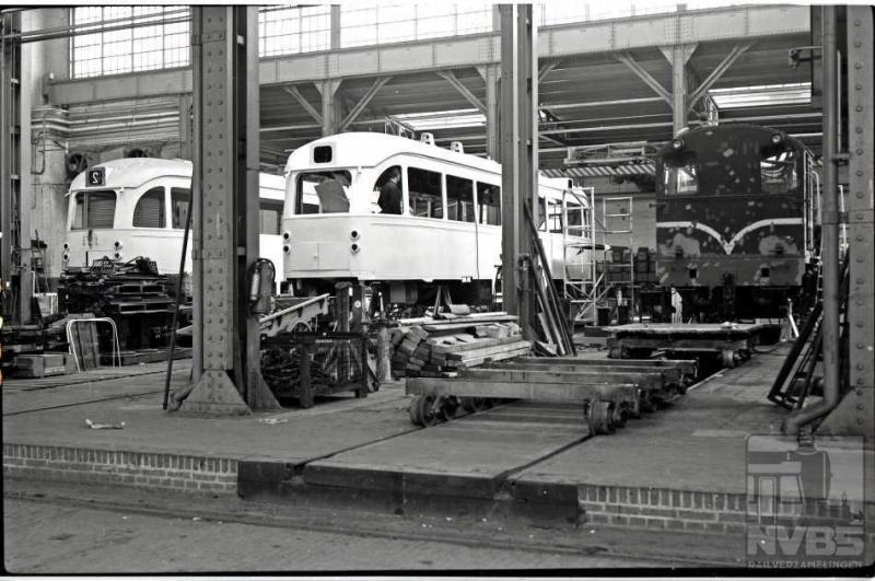 Dat in de werkplaatsen van NS niet alleen onderhoud aan het eigen materieel werd gepleegd, bewijst deze foto. De PCC-rijtuigen van de HTM kregen in de centrale werkplaats Tilburg een midlife-revisie. Op de foto worden de 1117 en 1187 onder handen genomen. Normaliter gingen de PCC's na deze revisie nog ruim vijftien jaar mee waarna onherroepelijk sloop volgde. Niet voor de 1187 echter: via omzwervingen onder andere naar Amsterdam kwam deze terug in Den Haag om daar alsnog, na van alle bruikbare onderdelen verlost te zijn, in 2013, te worden gesloopt. Naast de PCC-rijtuigen ontwaren we nog een voertuig van de NS: een rangeerlocomotief uit de serie 500. 17-4-1974. (Volgens mij hebben we hier te maken met een spiegelbeeldfoto!)(J.A.Bonthuis; 109.686C)