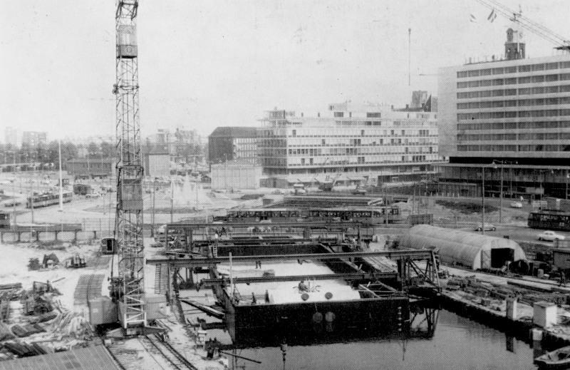 Een tunnelstuk voor het station Stadhuis wordt naar zijn definitieve plaats versleept. Op de achtergrond het Hofplein, het drukste kruispunt in de binnenstad. Op een tijdelijke brug over het kanaal rijdt een tram van het Hofplein naar het Weena.Juli 1963; prentbriefkaart uitgegeven door het RET-mannenkoor; verzameling SNR