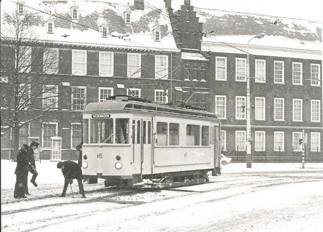 De serie motorwagens 290-299 (werkspoor; 1929) van de HTM werd in 1963/64 in haar geheel omgebouwd tot pekelmotorwagen. De H5 (ex-295) op het Buitenhof moet op Oudjaarsdag van 1978 even stoppen voor een vastgevroren wissel. Een lange reeks van zachte winters en de komst van dieselvoertuigen maakten de pekeltrams overbodig en dus gingen de meeste naar de sloper. De H5 op deze foto echter niet: er was weer eens een strenge winter geweest en de tot het bestand van het Haags Openbaarvervoermuseum (HOVM) behorende H5 werd ijlings voorzien van een nieuwe blauwe tank en door de HTM weer ingezet. Waarschijnlijk niet voor lange duur, want een moderne opvolger heeft zich al aangediend…De foto is gemaakt door P.E.Muré.