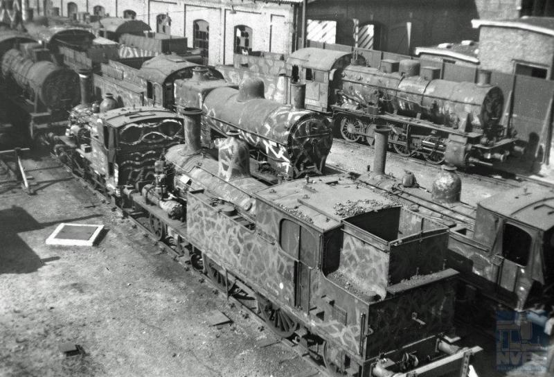 Zondag 17 september 1944 had de regering in Londen het bevel tot de spoorwegstaking gegeven waar op de meeste plaatsen in Nederland gehoor aan werd gegeven. De stoomlocomotieven die er nog waren, met camouflagebeschildering, werden bij de stations gestald zoals op deze foto naast de locloods van station Den Haag Staatsspoor. We zien locomotieven van de series 5500, 7700 en 3700. Op de achtergrond een G8-locomotief, een van de latere serie 4101-4149. (foto 509.025; 13-5-1945)