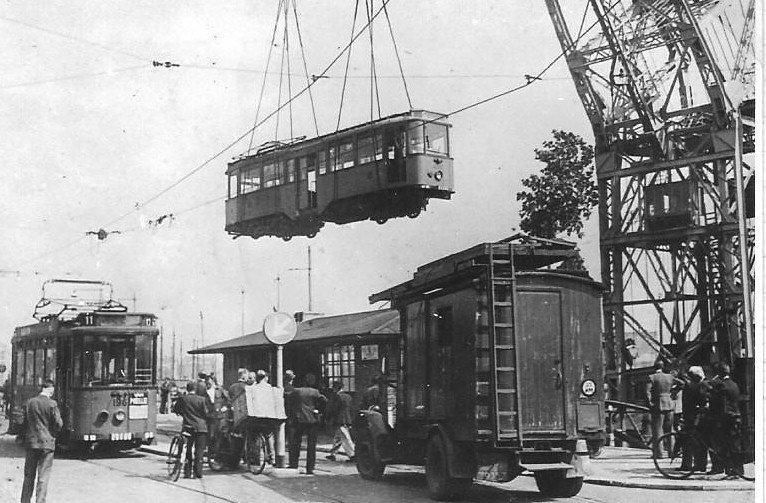 Door de nazi's gevorderde tramrijtuigen kwamen grotendeels weer naar Nederland terug: in Rotterdam gebeurde dit ook per schip. Met een kraan worden de trams uit het ruim getild en op de rails in de stad gezet. Motorwagen 196 staat er al en vierasser 450 bungelt nog in de lucht maar zal weldra de 196 vergezellen. Beide rijtuigen kwamen na een opknapbeurt weer in de normale dienst. (onbekende fotograaf; 23-5-1945)
