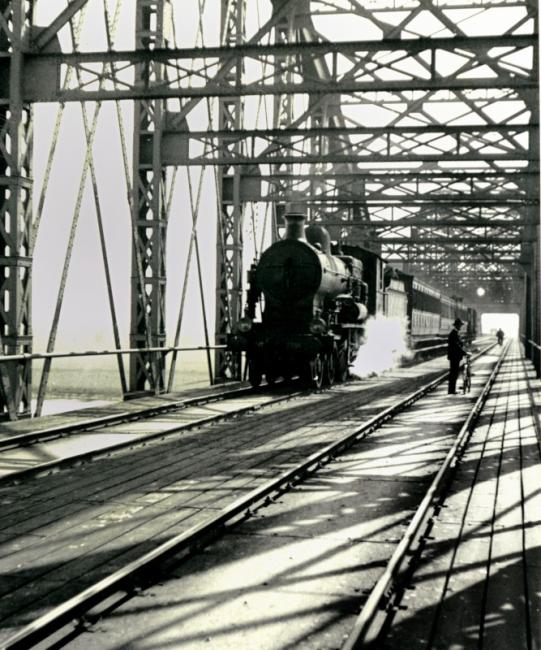 Spoorbrug in Rhenen, loc serie 3500 (ex NBDS) met sneltrein. De foto dateert uit 1936.De brug was onderdeel van de verbinding van Amsterdam naar Duitsland via Amersfoort, Nijmegen en Kleef, door de HSM ingesteld als concurrent voor de verbinding via Arnhem.De brug is in de 2e wereldoorlog vernield en na de oorlog niet meer hersteld.
