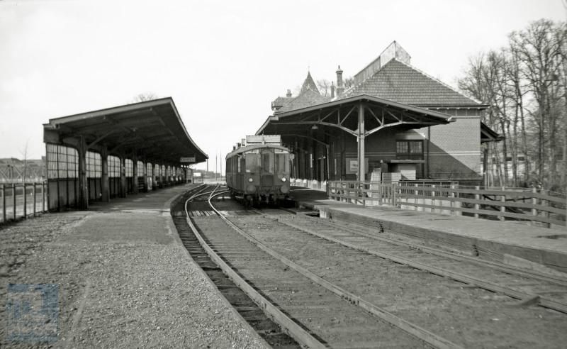 Gezicht op benzinemotorrijtuig NS omBC 1905 naast het perron van het uit 1911 daterende station Kampen. Links op de foto is de brug over de IJssel zichtbaar, die het station met de stad verbindt. Het motorrijtuig behoort tot de door Werkspoor gebouwde serie omBC 1904-1910 met DWK motor, in 1929 in dienst gesteld voor de Woldjerspoorweg tussen Groningen en Delfzijl. Het rijtuig sleet na de oorlog zijn laatste jaren rond Zwolle en zal in 1951 worden afgevoerd, maar pas in 1969 gesloopt, nadat het eerst nog als noodwoning heeft gediend.De perronkap links is er niet meer, en er rijden nu moderne treinen, maar verder is er aan het station niet veel veranderd.