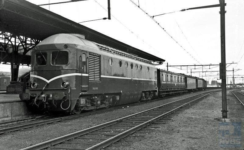 Diesellocomotief NS 2601 met een reizigerstrein uit Venlo langs het perron van station Eindhoven. Dit locomotieftype stond bekend als ′Beelen′ vanwege hun gelijkenis met het (kale) hoofd van de heer L.J.M. Beel, minister-president in 1946-1948 en 1958-1959. De locs zijn gebouwd door Werkspoor; vanwege veelvuldig optredende defecten werden de locs al na vijf jaar buiten dienst gesteld.Achter de loc een rijtuig serie B 6400.