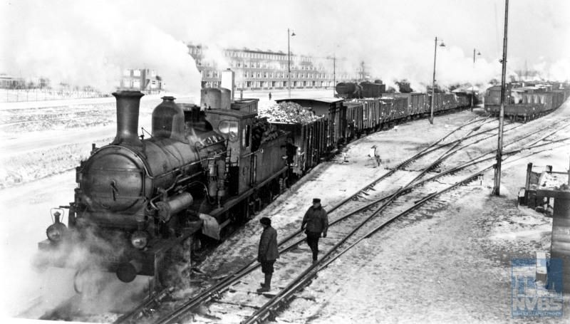Stoomlocomotief NS 3315 met een goederentrein in de sneeuw, met bij de locomotief twee rangeerders op het emplacement IJsselmonde.Dit emplacement was een belangrijk knooppunt waar treinen van en naar de Rotterdamse haven werden samengesteld.