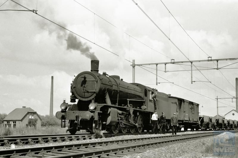 28 mei 1957: de laatste stoomtrein passeert Olst. Het gaat hier om een lege grindtrein 21387 die samen met zijn personeel poseert.De grindwagens dienden voor ballastgrind dat gedolven werd langs de Maas bij Linne. Achter de loc een houten goederen­trein-bagage­wagen ("Dg").