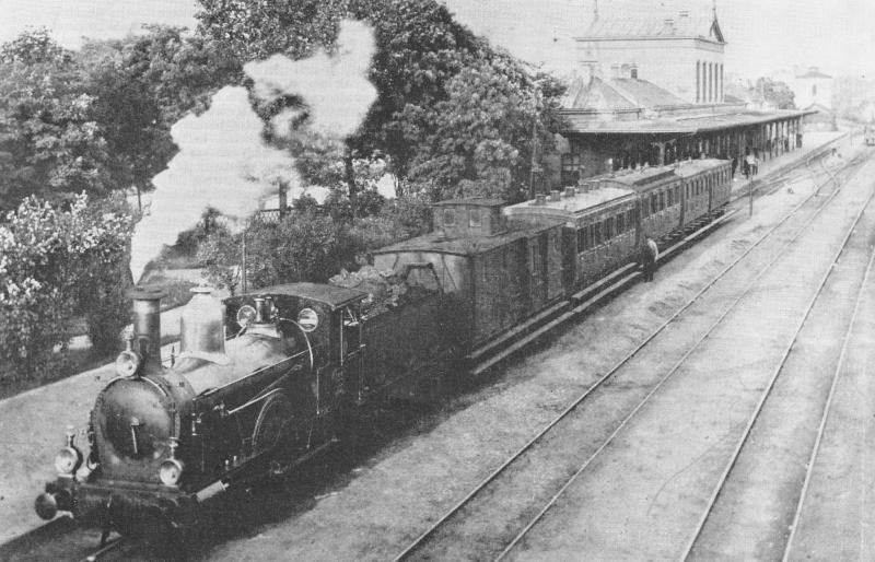 Hengelo is al aan zijn vijfde station toe. Nadat er ruim een jaar een tijdelijk station had gestaan, werd in 1866 een Waterstaatstation 3e klasse geopend, een hoofdgebouw, twee vleugels en twee eindgebouwen. Eenzelfde soort station werd gebouwd in Enschede en Meppel. Dat laatste staat er nog steeds. Met het oog op de toenemende hinder voor het wegverkeer werd in 1899 het hele emplacement opgehoogd; er stond van 1898 tot 1900 weer een tijdelijk station. In 1899 verscheen er een rijk gedecoreerd neo-renaissancistisch aandoend stationsgebouw met torentjes, ontworpen door G.W. Van Heukelom. De stationskap werd in 1900 geplaatst. Na de verwoesting van het stationsgebouw door een bombardement in 1944 kwam in 1951 het huidige gebouw tot stand. Foto: Het Waterstaatstation 3e klasse van Hengelo in de zomer van 1892; trein met SS-loc 133. 1892 (Foto: D.J. Boom - verz. NVBS Railverzamelingen - 644.961C)