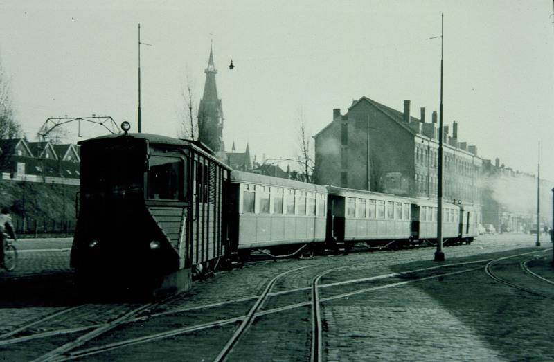 Een personentram komt aan bij het station aan de Rosestraat. Daarbij kruist hij het NS-goederenspoor dat van het emplacement IJsselmonde naar de BlueBand-fabriek liep.De tram wordt getrokken door de M67.