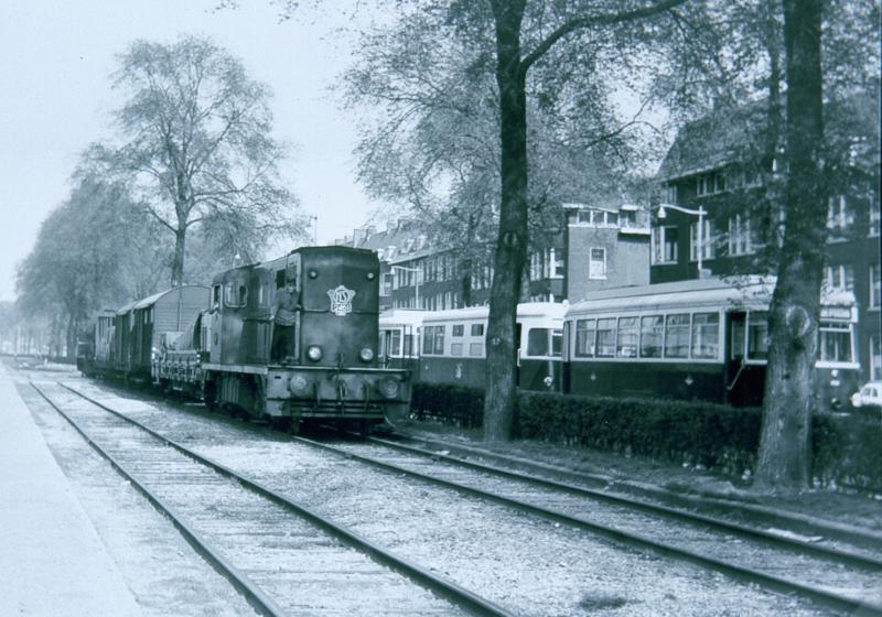 Op de Brielselaan zien wij een goederentrein van NS, getrokken door de 2461, samen met een tram van de RTM (het ′Sperwer′-stel).Op de Brielselaan lagen naast elkaar sporen van NS, van de RTM en van de Rotterdamse Electrische Tram (het stads­vervoer­bedrijf van Rotterdam).Foto: J.C. de Jongh, 11 maart 1965.