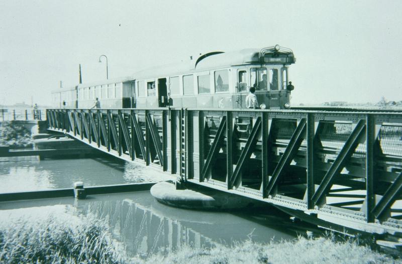 Na het passeren van de dorpen Geervliet en Heenvliet nadert de tram het Kanaal door Voorne. Hierover lag een draaibrug, die net breed genoeg was voor de tram, maar waar niettemin lange tijd al het verkeer overheen moest. In de nadagen van de tram is er voor het gewone verkeer een ophaalbrug naast gebouwd.Foto: J.W. Sluiter, 15 juli 1959.