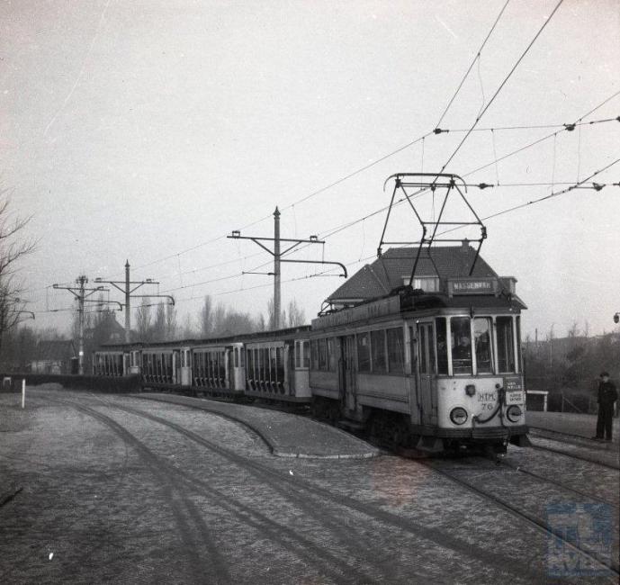 We blijven nog even bij de HTM, midden in oorlogstijd. Dat is ook te zien aan het verveloze uiterlijk van de interlokale motorwagen 76, die op deze plaat vier open aanhangers naar Leiden brengt, hier ter hoogte van de Posthof. Door de brandstof­schaarste en de gevorderde fietsen kregen de trams en bussen van de HTM, maar ook elders natuurlijk, het extra druk. De open aanhang­wagens die normaal alleen in de zomer dienst deden, moesten nu ook in de overige jaargetijden de remise uitkomen. Om de reizigers tegen de ergste kou te beschermen had de HTM een order aan de firma Beijnes in Haarlem gegeven om deze rijtuigen om te bouwen tot gesloten wagens. Het transport van Den Haag naar Haarlem geschiedde geheel over tramrails. Op deze foto brengt emr.76 de 557, 555, 554 en 556 naar de NZH-remise aan de Rijnsburgerweg te Leiden, vanwaar de NZH het verdere transport voor haar rekening zou nemen. Het is 28 februari 1944. (J.A.Bonthuis; NVBS-fotonummer 109.502)
