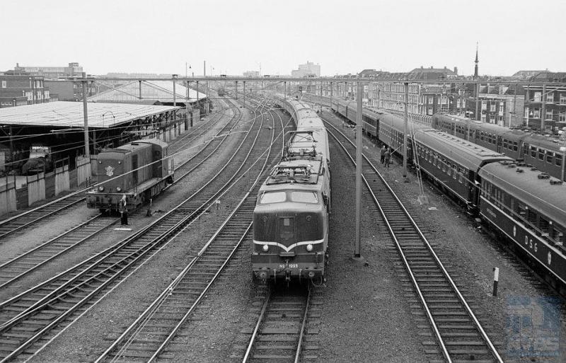 Op het emplacement van station Den Haag HS (Hollands Spoor) rijdt eloc 1223 met een reizigerstrein binnen, op weg van Venlo naar Amsterdam. Links zien we dieselloc 2492 staan. De rijtuigen rechts worden met de hand gewassen; zij behoren tot een trein van een reisbureau; vooraan een slaaprijtuig van de DSG (Deutsche Schlafwagen Gesellschaft). Nog meer naar rechts een stroomlijntreinstel. Veel te zien dus op deze foto, die R. Ankersmit op 17 juni 1961 heeft gemaakt (NVBS-fotonummer onbekend).