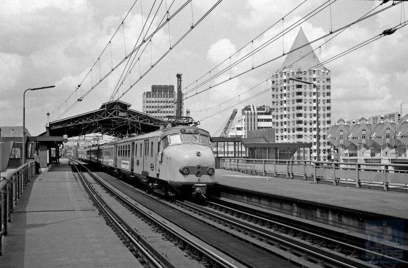 Vanaf 1956 komt er wederom nieuw elektrisch reizigersmaterieel op de rails: het zogenaamde ′mat 54′ of te wel Hondenkoppen. Oorspronkelijk groen geschilderd met rode accenten, zijn zij op deze foto al slachtoffer geworden van de openbaarvervoergeelrage. Die duurde gelukkig niet al te lang. Op deze foto zien we twee treinstellen van het type ElD2; er waren echter ook vierdelige Hondenkoppen. De locatie is het station Rotterdam Blaak waarvan de kap goed zichtbaar is met ernaast het markante flatgebouw en de kubuswoningen van architect Blom. J.A.Bonthuis heeft de foto op 2 juni 1989 geschoten (NVBS-fotonummer 5425.506).
