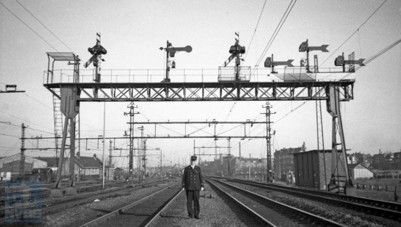 Wie de NS-er is op deze foto, is onbekend, maar dat hij een voorliefde heeft voor het seinwezen is overduidelijk. Deze seinbrug bij Rotterdam DP-Aansluiting overspant de sporen tussen Rotterdam DP en Schiedam/Rotterdam RMO (RechterMaasOever). In de dertiger jaren waren nog niet zo heel veel spoorfotografen actief, maar H.G.Hesselink gelukkig wel: ook deze foto is door hem genomen en wel op 20 februari 1936. (NVBS-fotonummer 170.531).