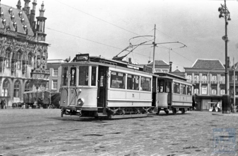 Eveneens op de Markt lag het beginpunt van de elektrische tramlijn van Middelburg naar het station in Vlissingen. Links is nog een deel van het fraaie laatgotische stadhuis te zien. Motorrijtuig 2 met aanhangwagen nummer x (het nummer is niet bekend en niet te lezen) staan klaar voor vertrek.
