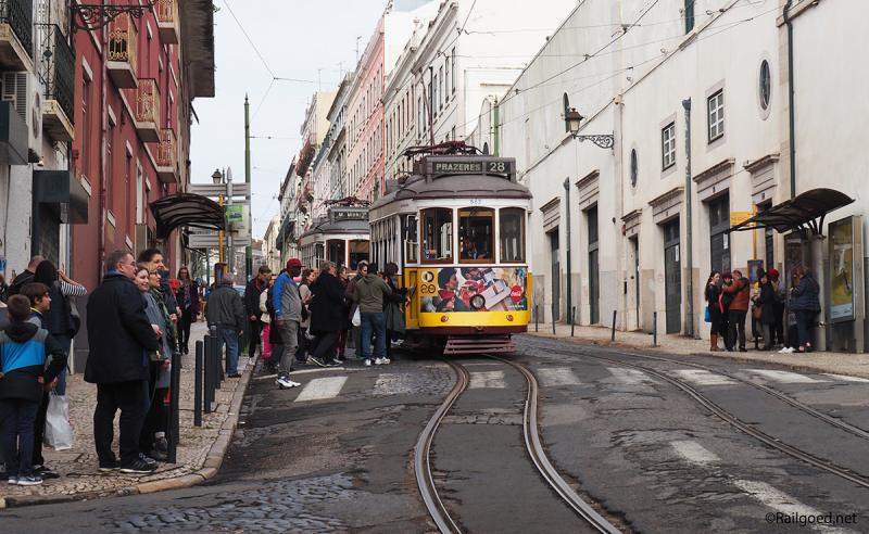 Twee trams van lijn 28E bij halte São Vicente, waar massa's mensen zich op de tram storten.