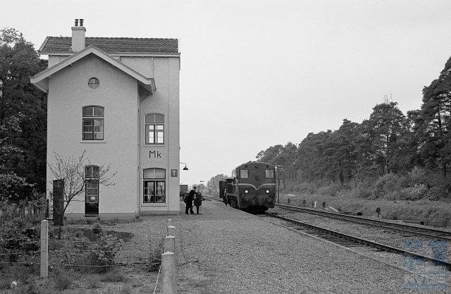 Station Markelo is evenals Laren-Almen niet meer in dienst, sinds 1953 al weer. Het lijkt bewoond en het heeft zijn oorspronkelijk witte kleur behouden. Het is een door K.H. van Brederode ontworpen Waterstaatstation 5e klasse. Bouwtechnisch heeft het dezelfde ontwikkeling doorgemaakt als het station Laren-Almen.Foto: Gezicht op het emplacement Markelo (km 24,3) met op spoor 1 goederentrein 4912 (Venlo - Enschede) bestaande uit locomotief NS 2202 en open goederenwagen DB 839261 met geïmporteerde kolen.6 mei 1961. (Foto: R. Ankersmit)