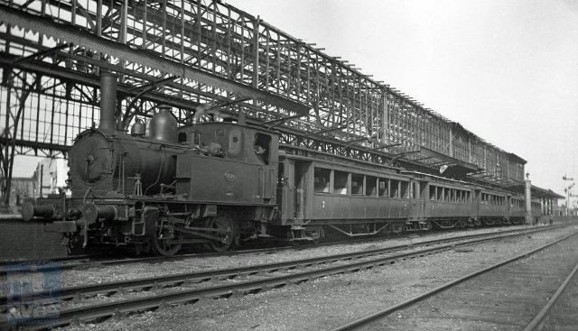 Locomotief NS 8126 is met vijf tramrijtuigen teruggekomen in Hengelo als reizigerstrein uit Enschede. De oorlogsschade is zichtbaar: van de perronkap is alleen nog de staalconstructie overgebleven en de rijtuigen hebben geen glas in de vensters. 15 juni 1945.(Foto W.D.J.Cramer - verz NVBS Railverzamelingen - NEG119-445)
