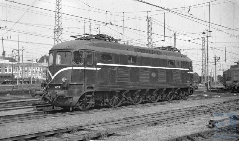 In 1948 komt de eerste serie elektrische locomotieven bij NS op de baan: de Duizenden. De eerste drie stuks zijn Zwitsers, gebouwd door Winterthur/Oerlikon maar de overige zeven puur Hollands: Werkspoor/Heemaf en Smit. De acht motoren ontwikkelden een behoorlijk continu vermogen van 3800 pk of te wel 2794 kW. De asindeling is (1A)Bo(A1). Ondanks het kleine aantal van tien stuks (1001-1010) kwam je ze door het hele land tegen. Tot 1982 dan, want toen gingen ze uit dienst. De 1002 op de foto is inmiddels blauw geschilderd en staat op het emplacement van Amsterdam CS. Het is 28 augustus 1954. Bonthuis was een expert in het maken van fraaie materieelfotoï¿&frac12s, getuige deze prent (NVBS-fotonummer 639.652).